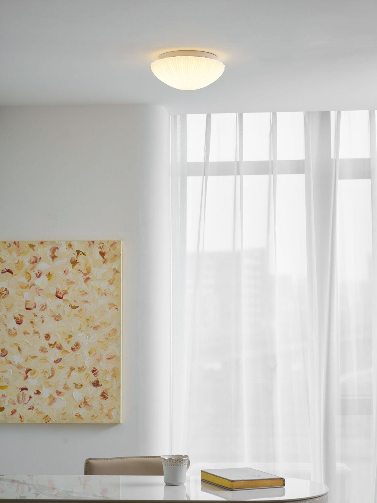 Small and glowing warm, this Clérachic ceiling light lights a room with sheer curtains and a framed painting.