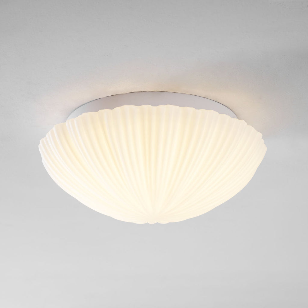 Stepped back for a wider view, this Clérachic ceiling light shows its full ribbed profile glowing warm against a grey wall.