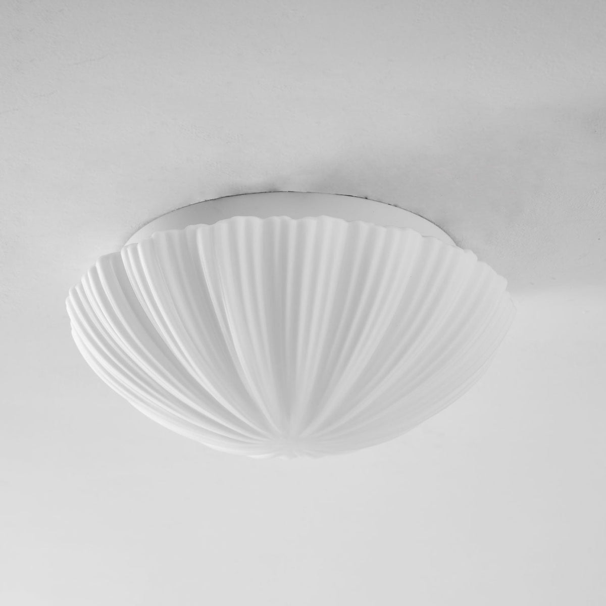 Unlit and shown in full, this Clérachic ceiling light's shell-shaped shade sits pale white against a grey backdrop.