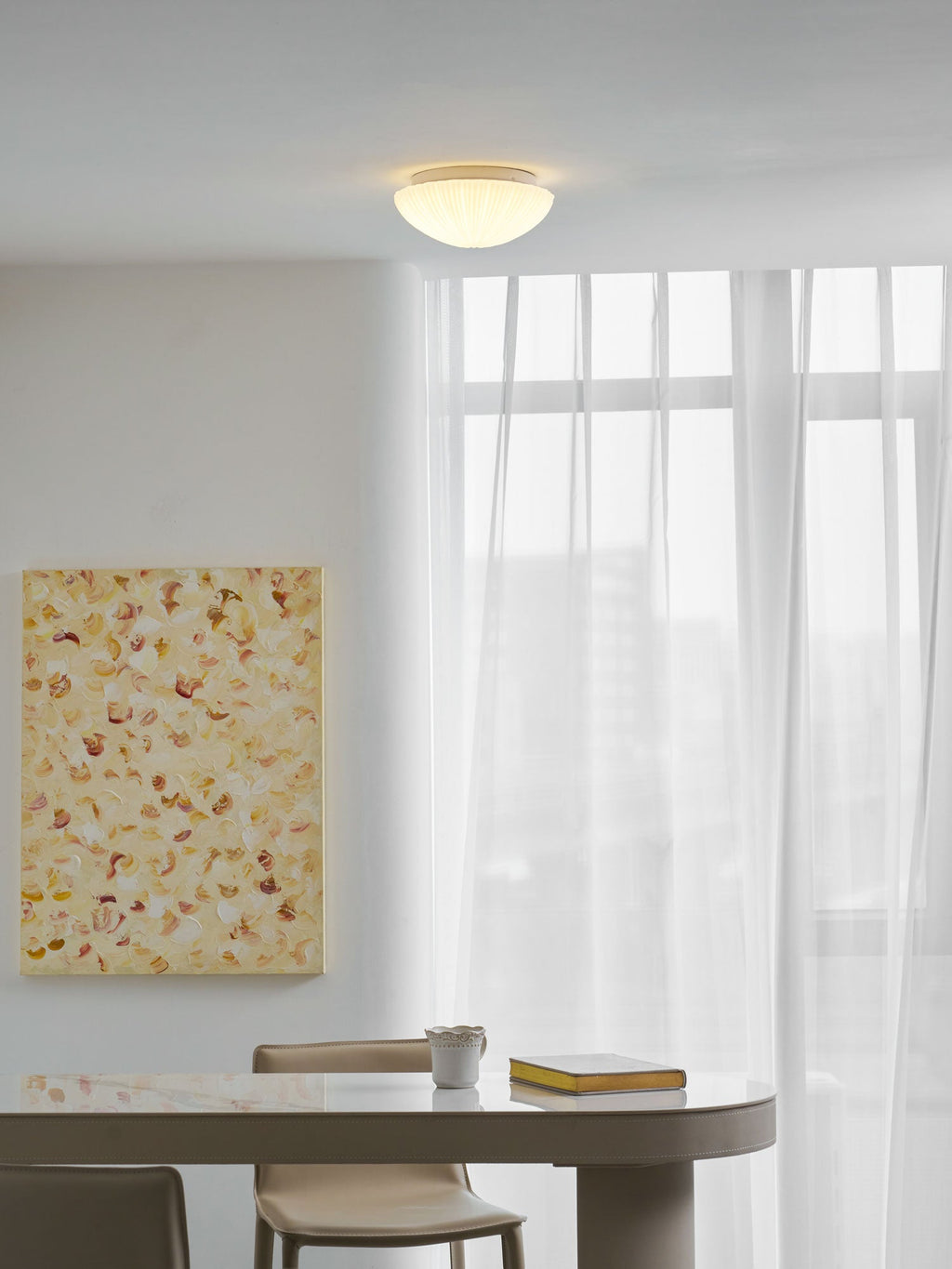 Above a table set with a mug and a stack of books, this Clérachic ceiling light glows warm white.