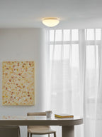 Above a table set with a mug and a stack of books, this Clérachic ceiling light glows warm white.