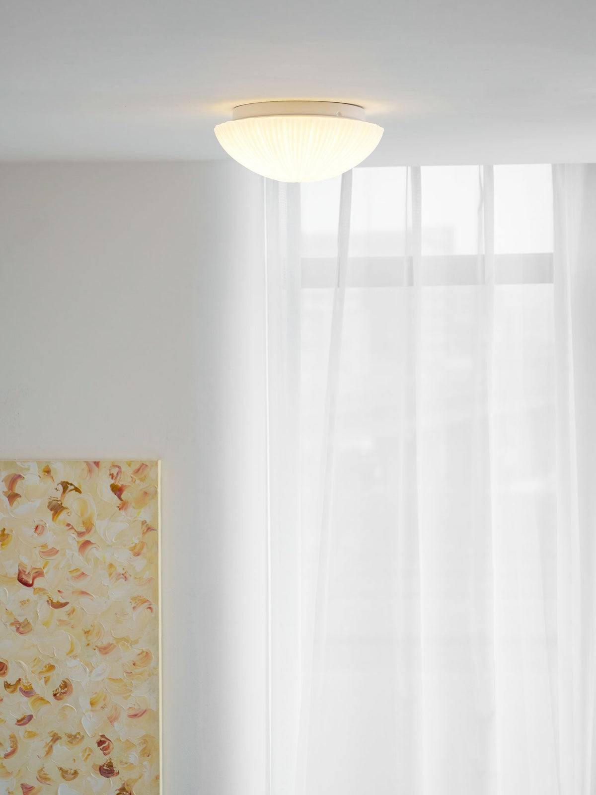 This Clérachic ceiling light glows softly above a room with tall windows dressed in sheer curtains.
