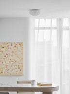 Over a round table holding a mug and an open book, this Clérachic ceiling light glows warm.