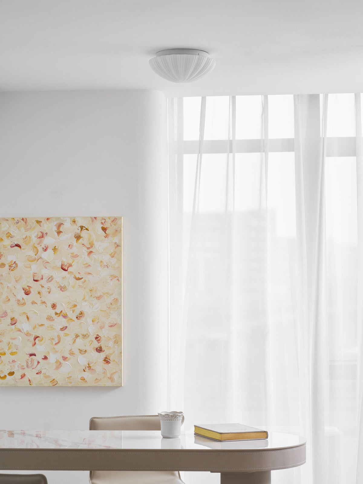 Over a round table holding a mug and an open book, this Clérachic ceiling light glows warm.