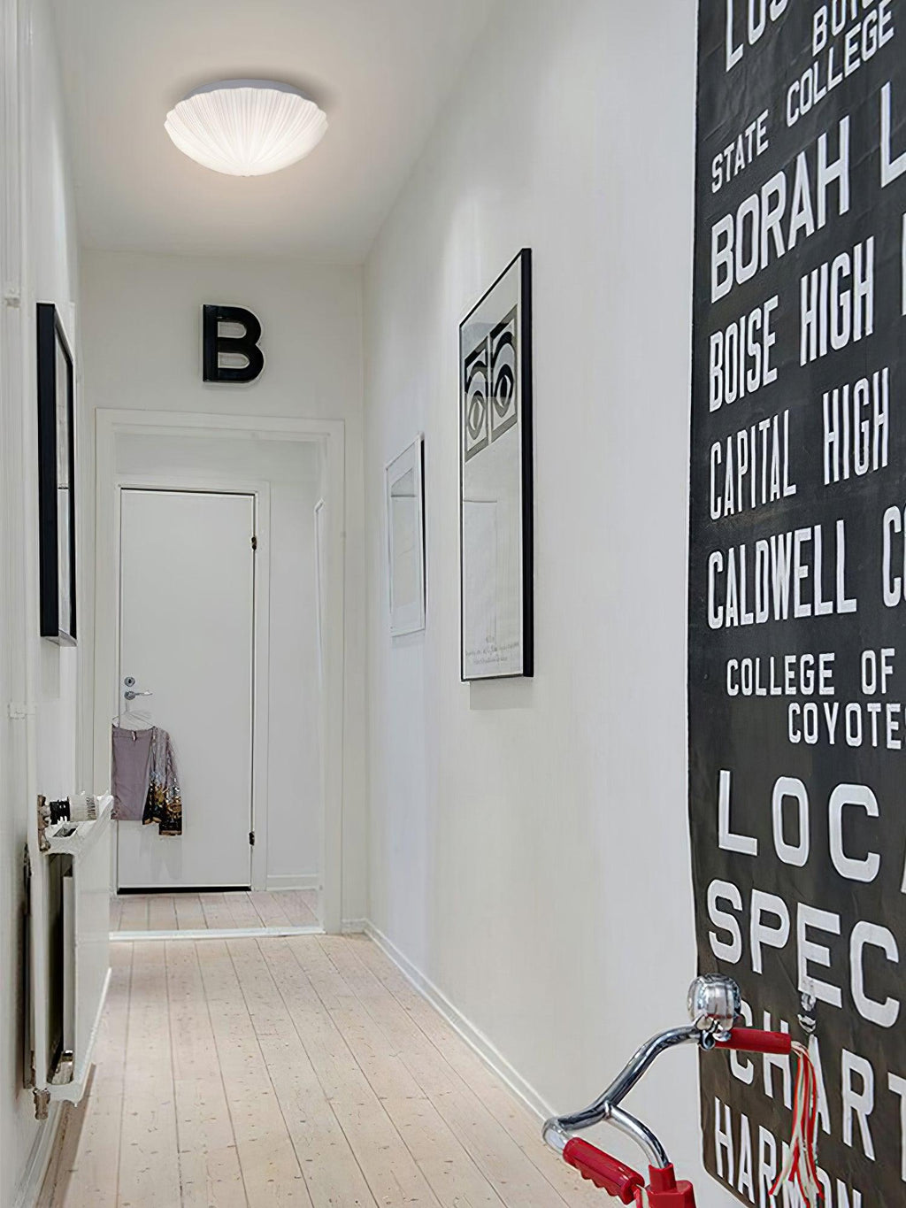 Dim and small on a hallway ceiling, this Clérachic light sits above a wall hung with lettered artwork.