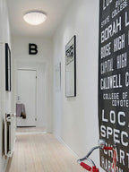 Dim and small on a hallway ceiling, this Clérachic light sits above a wall hung with lettered artwork.