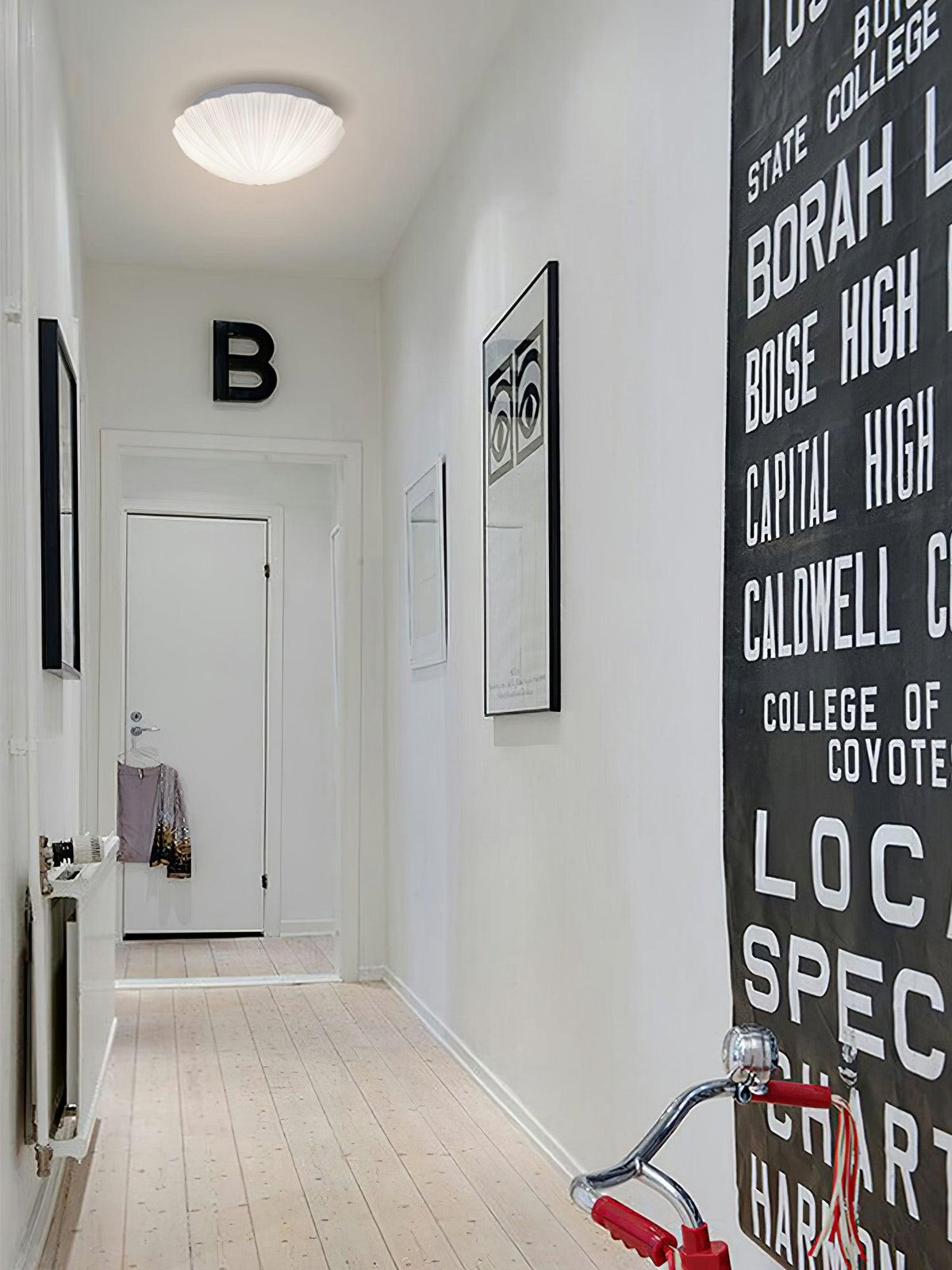 Dim and small on a hallway ceiling, this Clérachic light sits above a wall hung with lettered artwork.