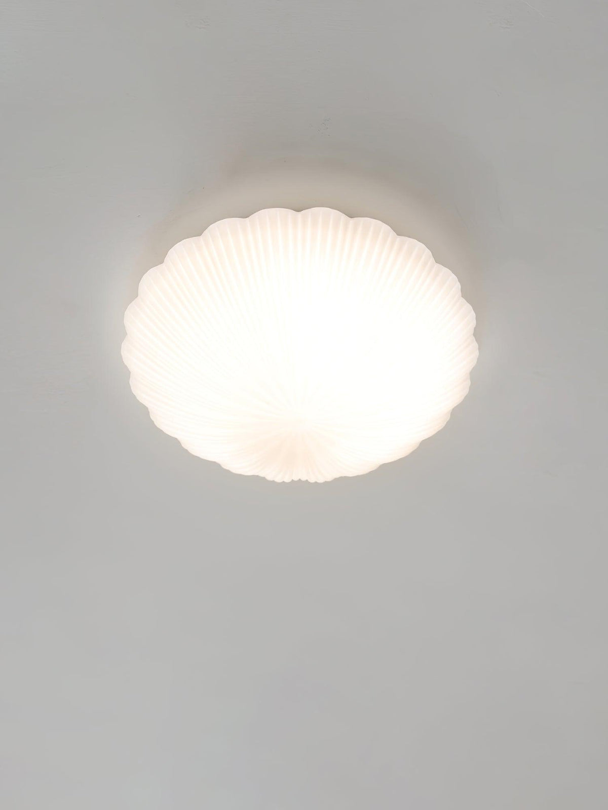 Front-on and lit, this Clérachic ceiling light glows warm white in a pale, softly lit room.