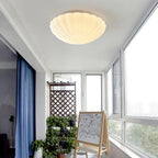 Warm light spills from the ribbed shade of this Clérachic ceiling light onto a room with a blue curtain.