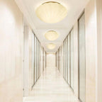 Three of this Clérachic ceiling light hang in a row along a marble-floored hallway, each glowing warm white.