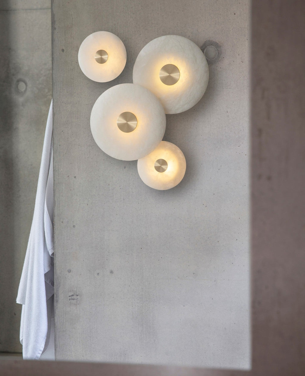 Tall view of the four-disc alabaster arrangement lit on a concrete pillar, towel hanging to the left.