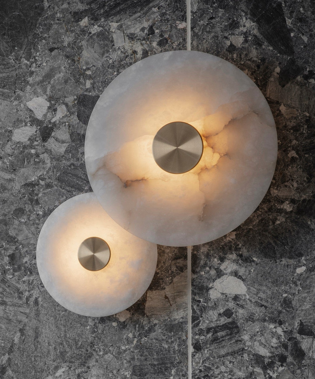 Two lit alabaster discs mounted on a dark grey marble wall, glow pooling through the stone.