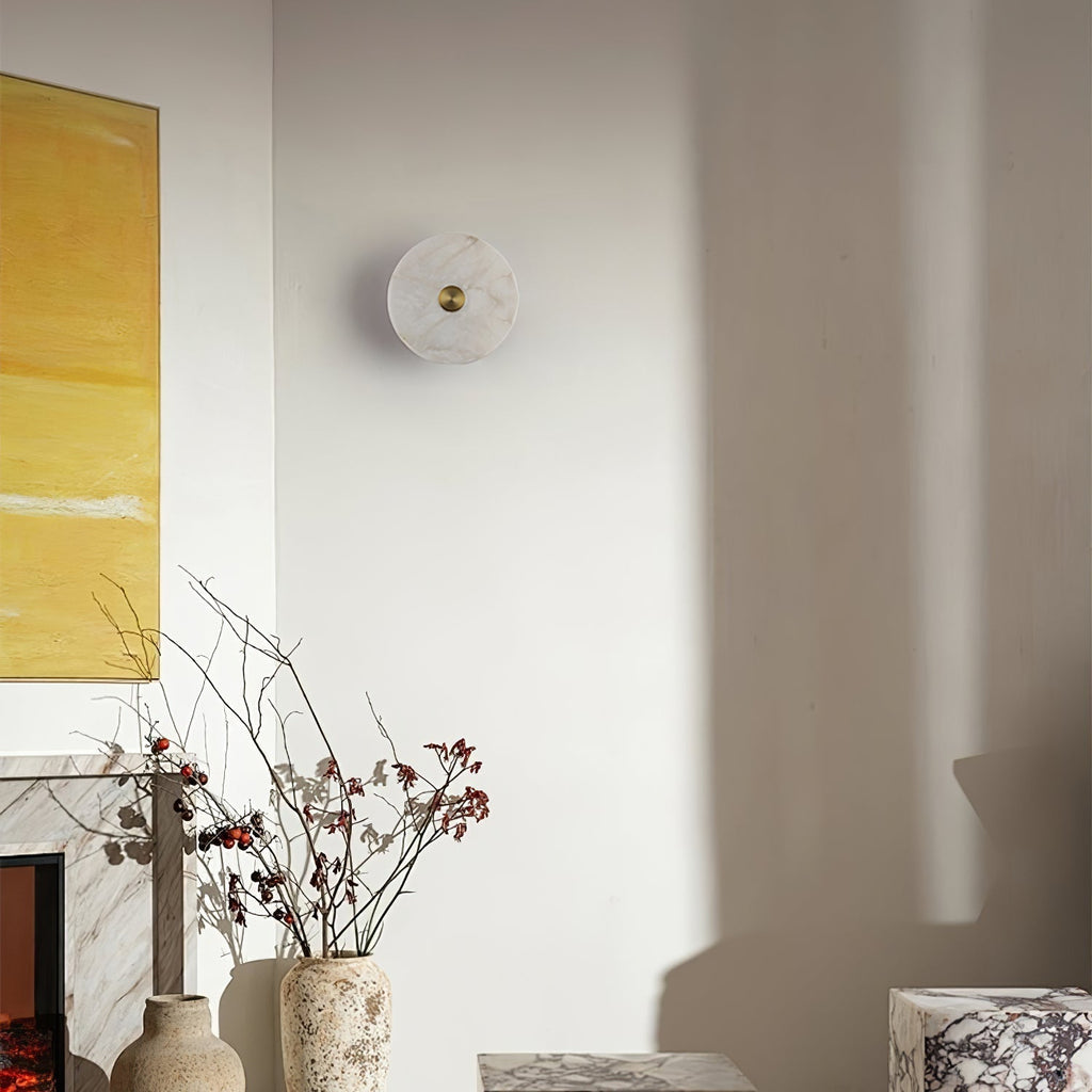 Unlit alabaster disc wall light in a living room corner, beside a fireplace and yellow artwork.