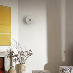 Unlit alabaster disc wall light in a living room corner, beside a fireplace and yellow artwork.