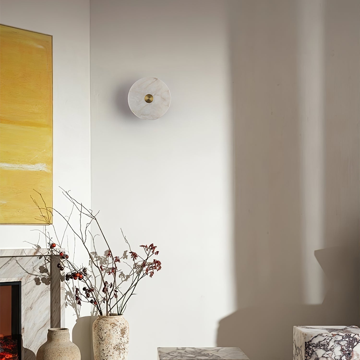 Unlit alabaster disc wall light in a living room corner, beside a fireplace and yellow artwork.