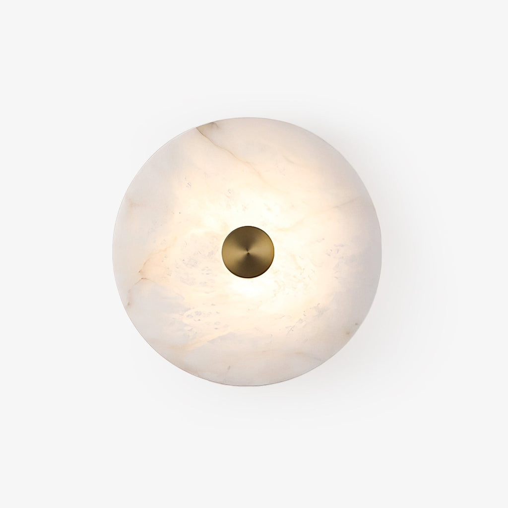 Studio shot of the lit alabaster disc sconce, brass cap centred on the marbled stone face.