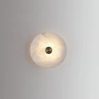 Single alabaster disc wall light lit on a plain grey wall, casting a soft halo around itself.
