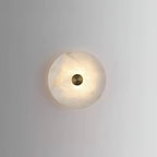 The alabaster disc sconce lit at close range, showing the cloudy grain of the natural stone.