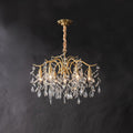 Brass chandelier on dark grey, clear crystal leaves hanging from curved arms below the ceiling plate.
