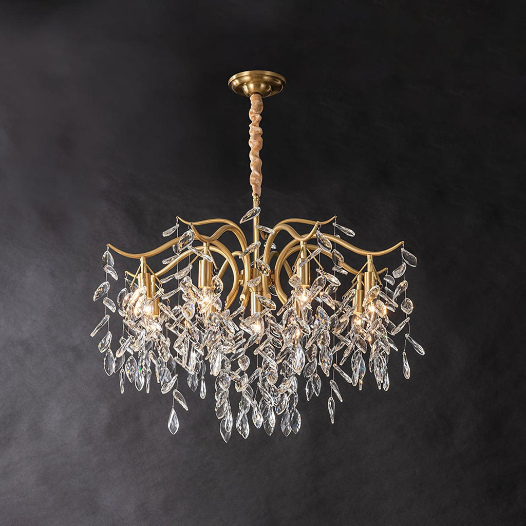 The same chandelier fuller on dark grey, more crystal leaves massed beneath the lit brass arms.
