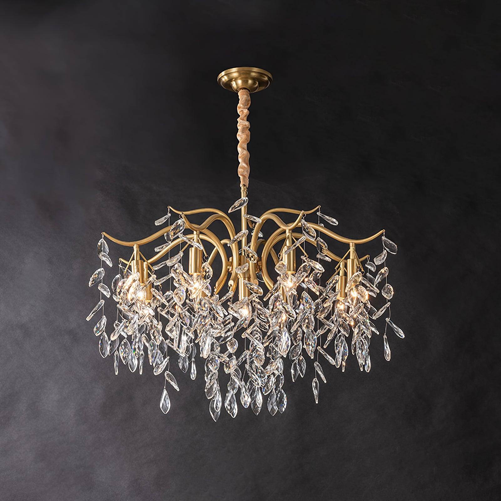 The same chandelier fuller on dark grey, more crystal leaves massed beneath the lit brass arms.