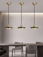 Three gold Clérachic pendant lights spaced along a wall above a dining table in a minimalist grey room.