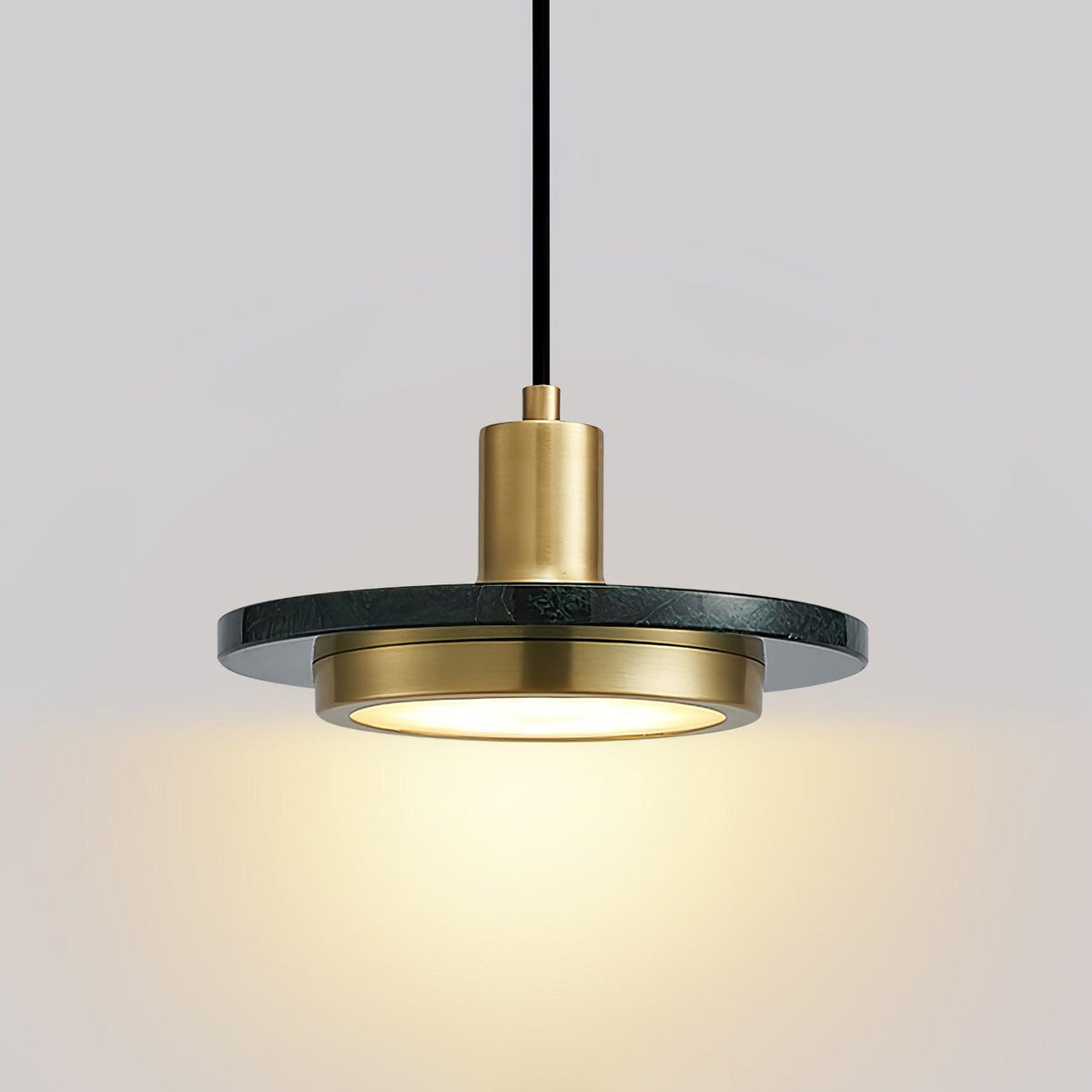Angled close-up of a Clérachic pendant light against grey, its gold socket and glowing disc catching the light.