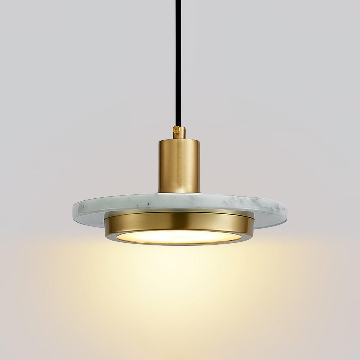 Close-up of a white marble Clérachic pendant light, its gold cylinder socket catching the light above the disc.