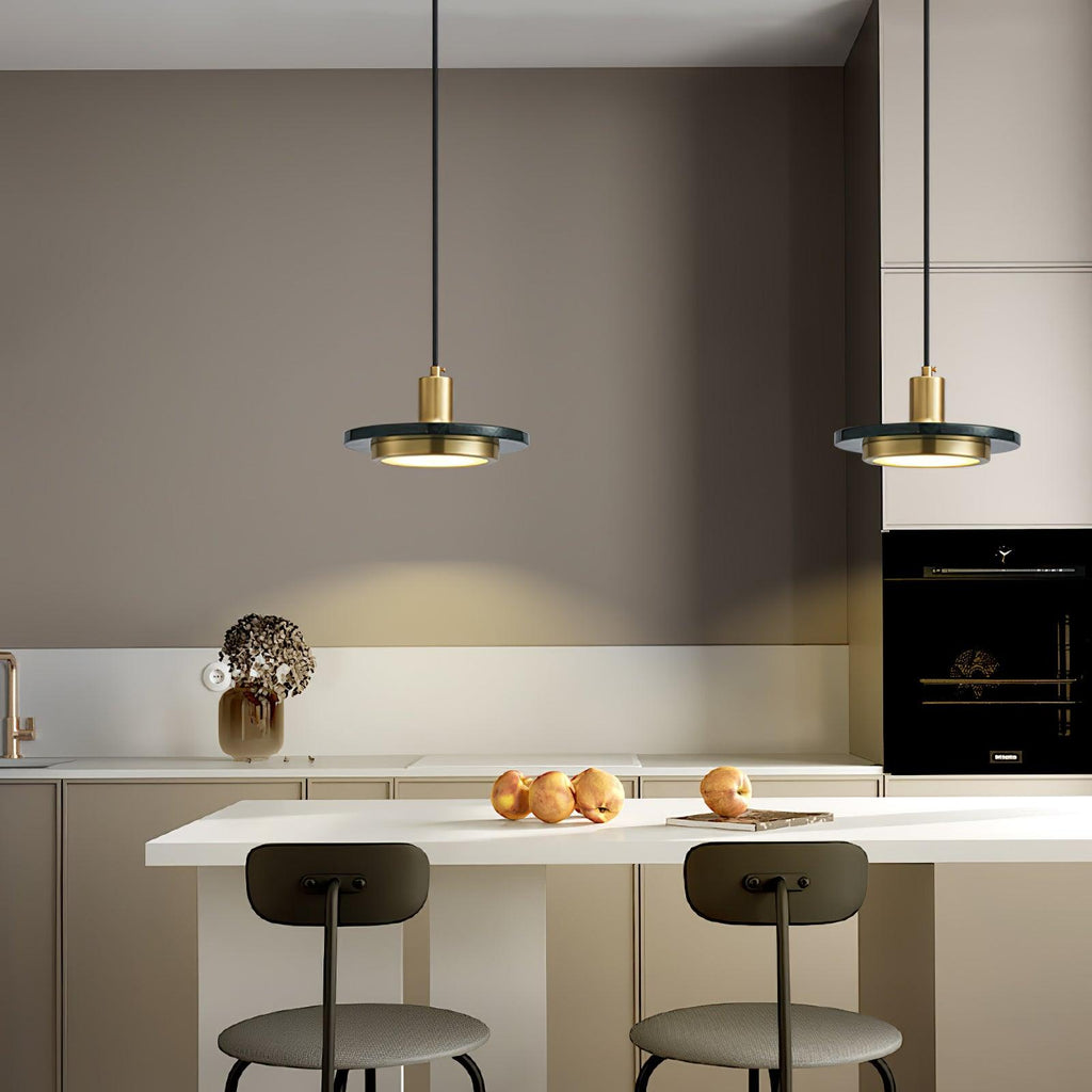 Two gold Clérachic pendant lights hang above a beige kitchen island set with bar stools and fruit.