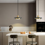 Two gold Clérachic pendant lights hang above a beige kitchen island set with bar stools and fruit.