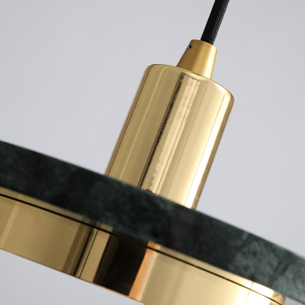 Macro shot of a Clérachic pendant light's gold cylinder set against the veined edge of its dark marble disc.