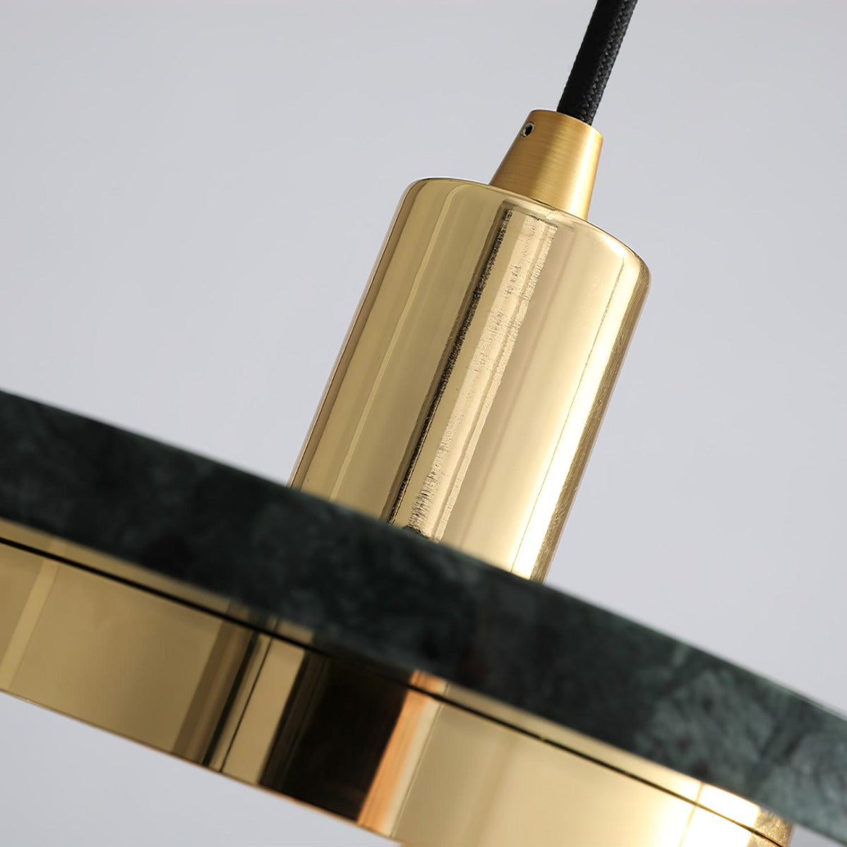 Macro shot of a Clérachic pendant light's gold cylinder set against the veined edge of its dark marble disc.