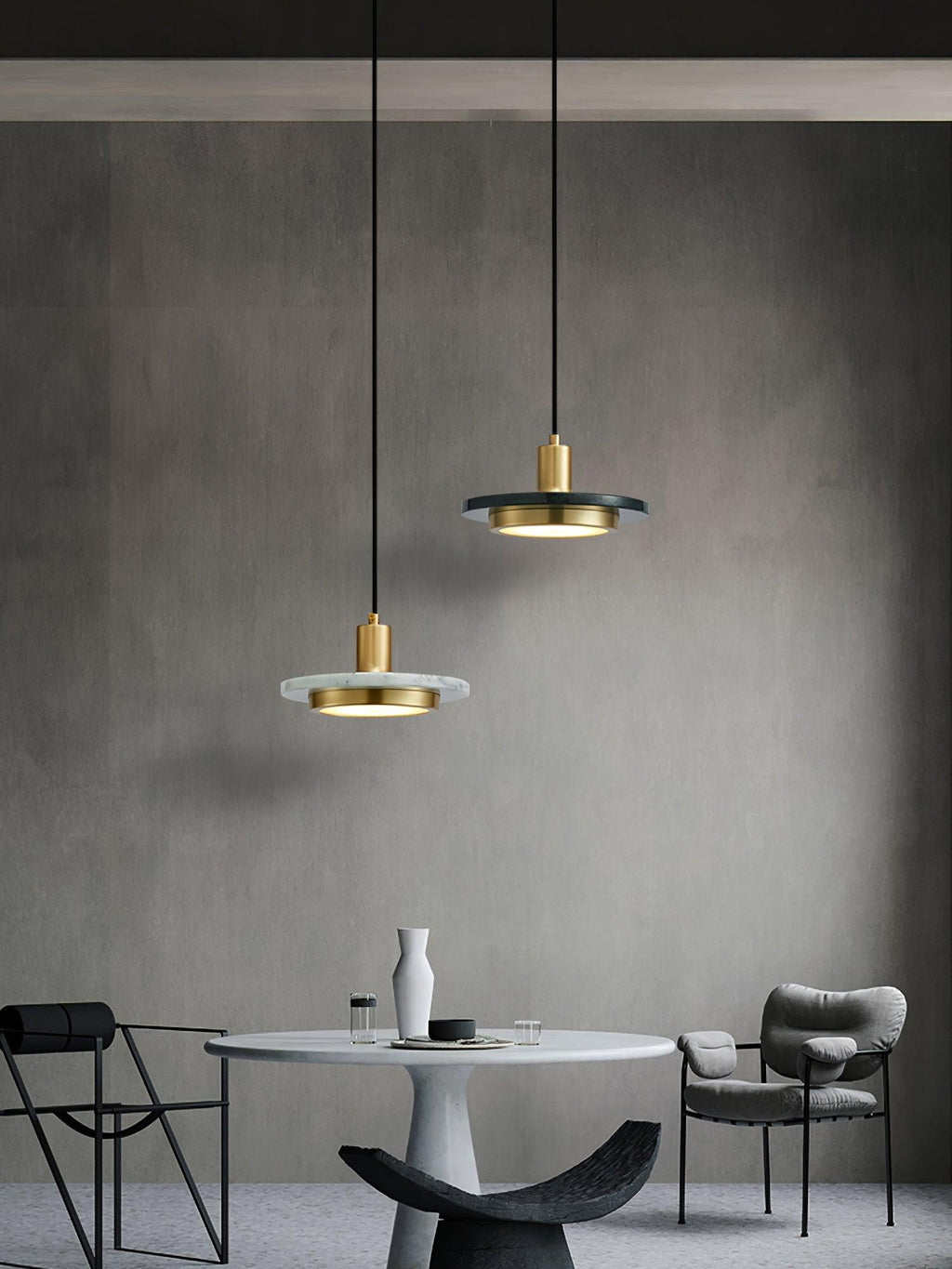 Two Clérachic pendant lights at staggered heights hang above a round table in a dark, minimalist room.