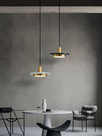 Two Clérachic pendant lights at staggered heights hang above a round table in a dark, minimalist room.