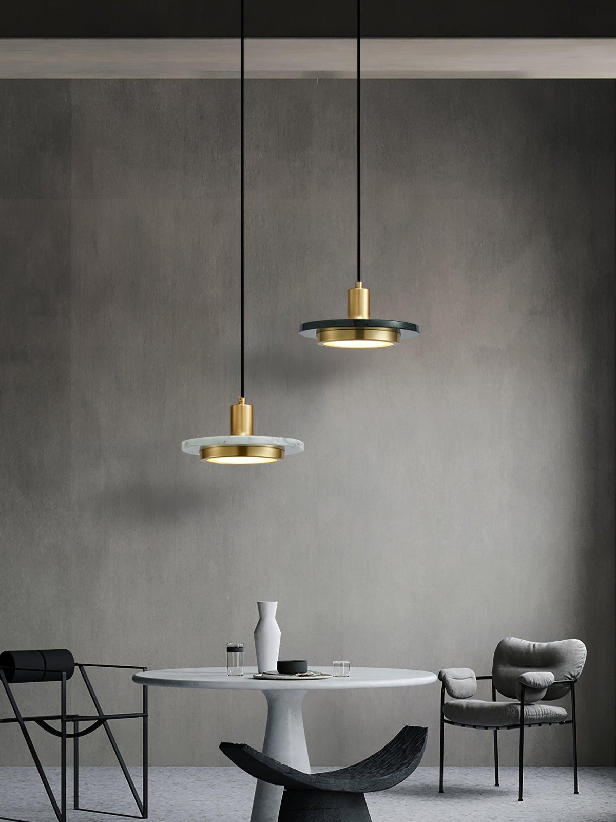 Two Clérachic pendant lights at staggered heights hang above a round table in a dark, minimalist room.
