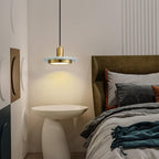 A Clérachic pendant light glows warm beside a bed with an olive-green headboard and a round side table.
