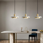 Three gold Clérachic pendant lights hang above a marble dining table with gold legs and a blue velvet chair.