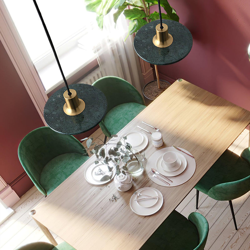 Overhead view of two green marble Clérachic pendant lights above a table set for dinner with green velvet chairs.