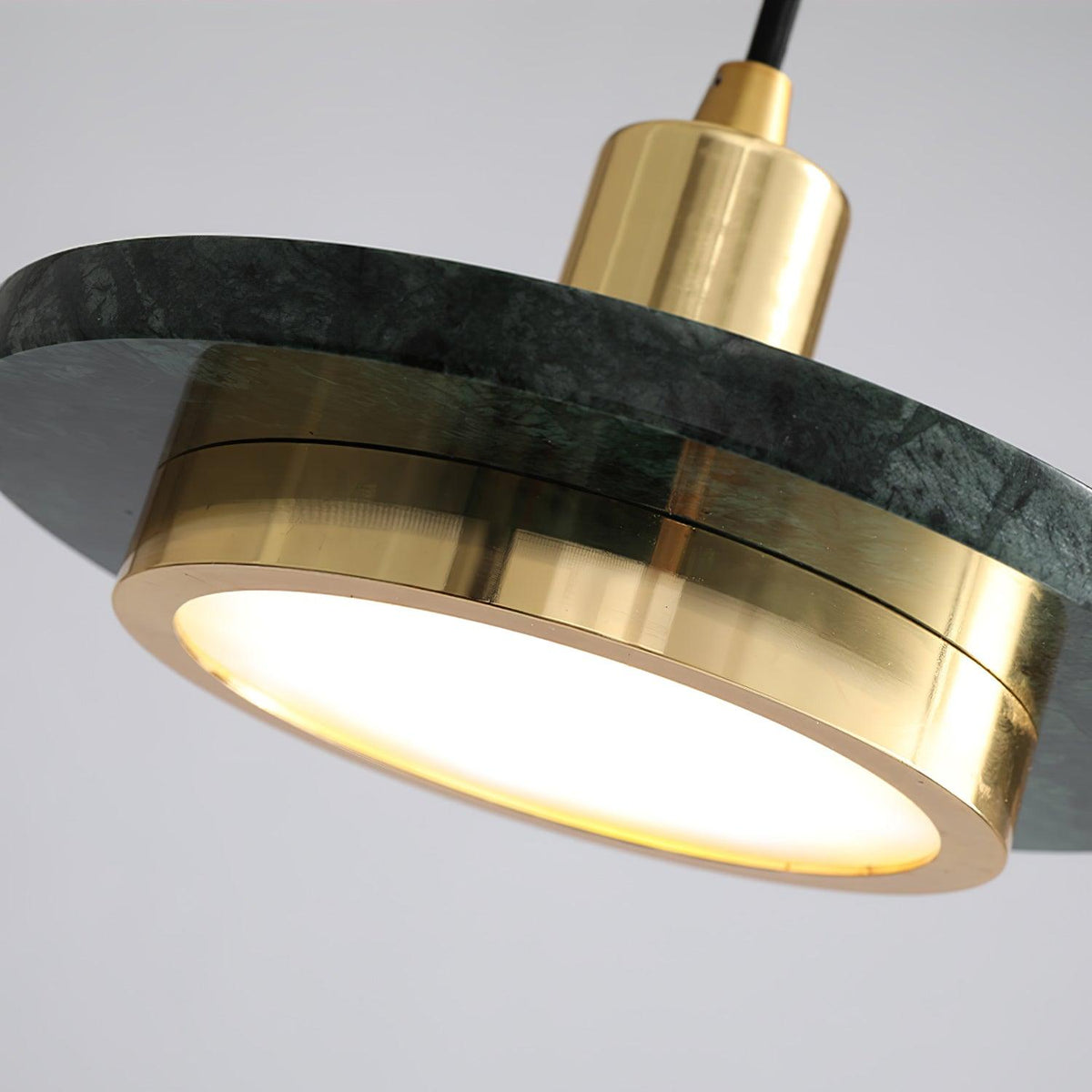Angled close-up of a green marble Clérachic pendant light's gold rim and glowing disc seen from below.