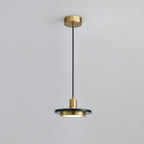 Clérachic pendant with a dark stone disc glowing softly beneath its brass fitting, framed closer on its cord against pale grey.