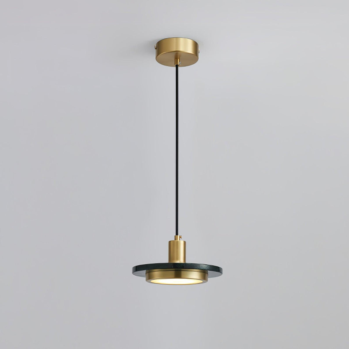 Clérachic pendant with a dark stone disc glowing softly beneath its brass fitting, framed closer on its cord against pale grey.
