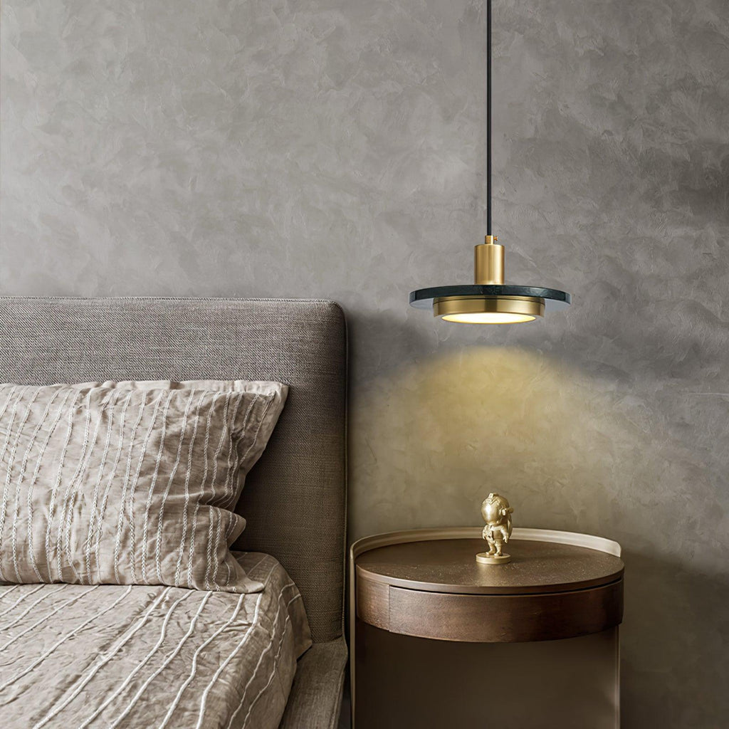 A Clérachic pendant light glows beside a beige upholstered bed, lighting a small figurine on the nightstand.
