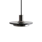 Underside close-up of a dark gunmetal disc pendant, angled to show its brass neck meeting the shade, shot on white for Clérachic.