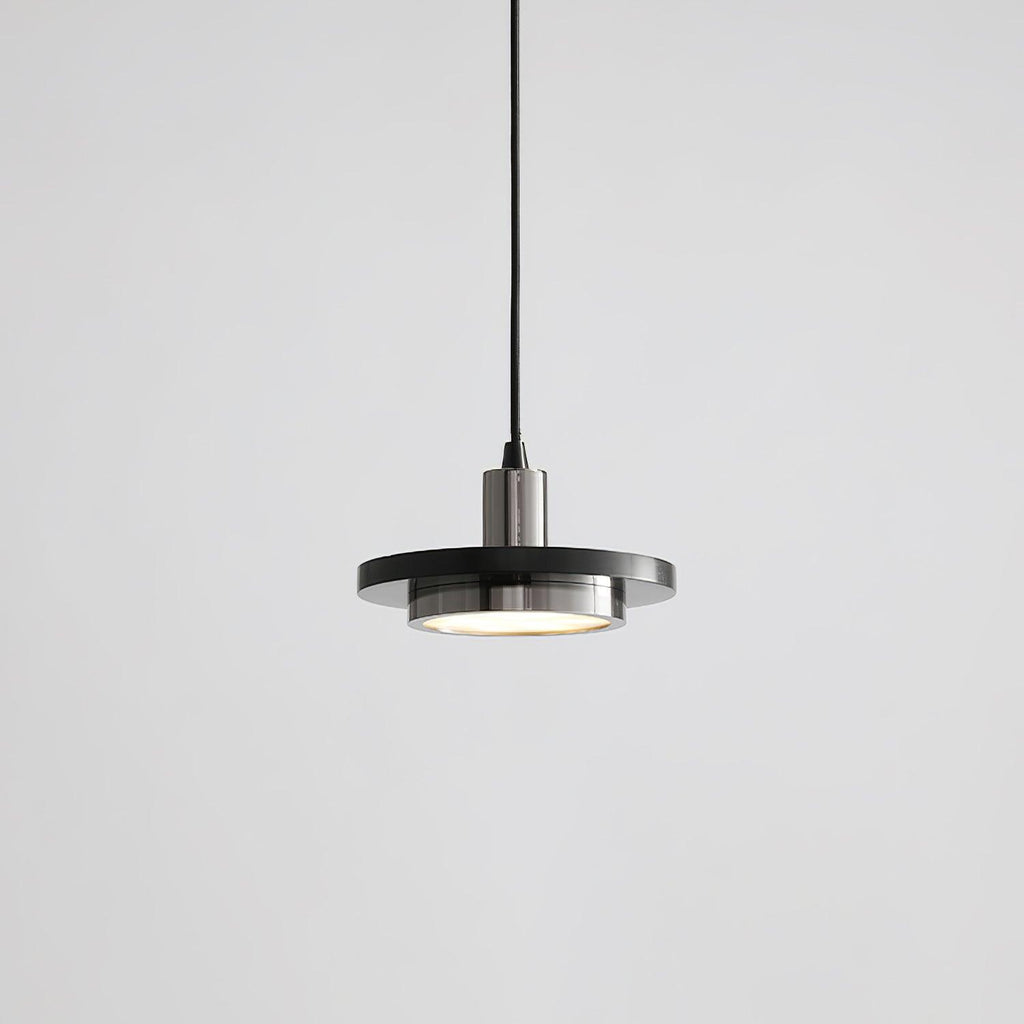 A matt dark disc pendant with a brushed steel-toned fitting drops on its black cord in this grey-background shot from Clérachic.