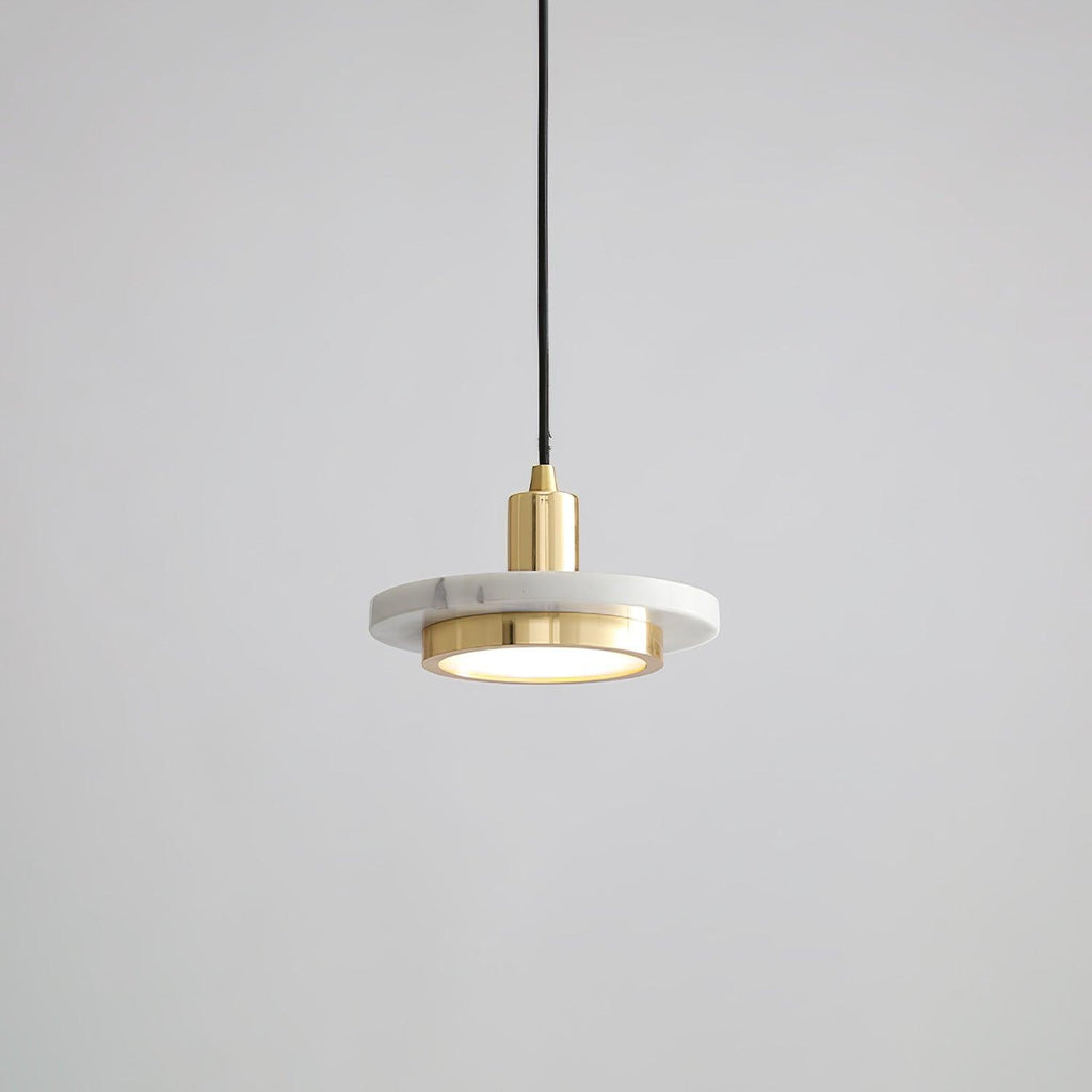 White marble disc pendant with a gold-toned rim caught mid-cord against grey, the Clérachic fixture's brass fitting bright at its centre.