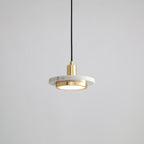 White marble disc pendant with a gold-toned rim caught mid-cord against grey, the Clérachic fixture's brass fitting bright at its centre.