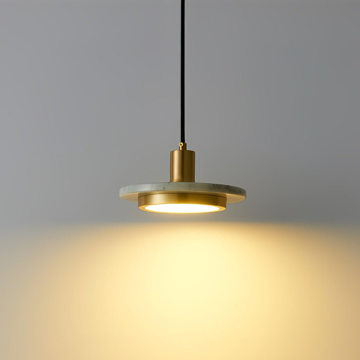 A single Clérachic pendant light against plain grey, its warm light spreading in a wide pool below it.