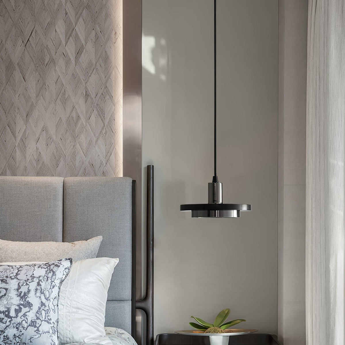 A black Clérachic pendant light hangs beside a grey tufted headboard and marble-pattern bedding.