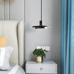 A Clérachic pendant light hangs beside a bed's white nightstand, wall sockets visible just above the headboard.