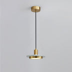A pale marble disc pendant hangs on a long black cord from its brass ceiling plate, photographed full length by Clérachic against soft grey.